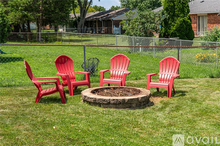 Four red chairs are arranged around a fire pit in a grassy yard.
