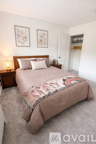 A bedroom with a bed, two pictures on the wall, a nightstand with a lamp, and a door.