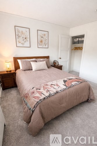 A bedroom with a bed, two pictures on the wall, a nightstand with a lamp, and a door.