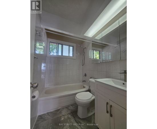 A white toilet sits in a bathroom with a white tub and sink.