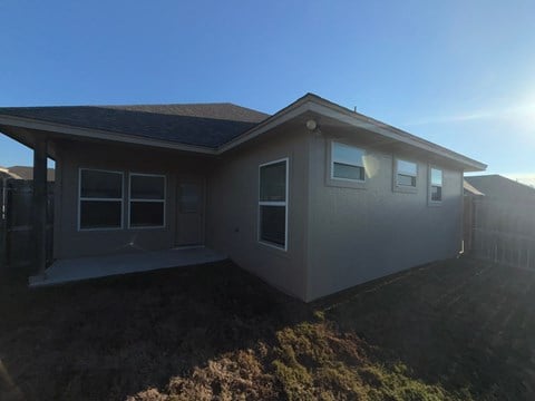 A house with a brown roof and white walls is surrounded by a grassy area.