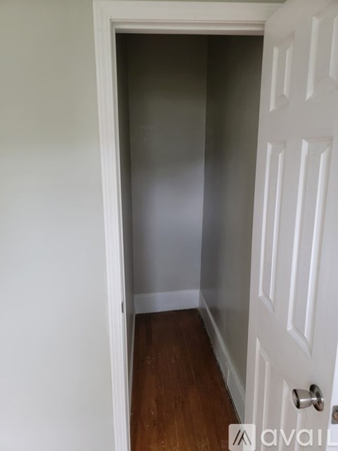 A white door with a silver handle is in a room with a wooden floor and white walls.
