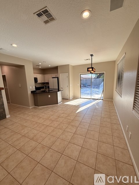 A spacious living room with a kitchen in the background and a large window letting in natural light.