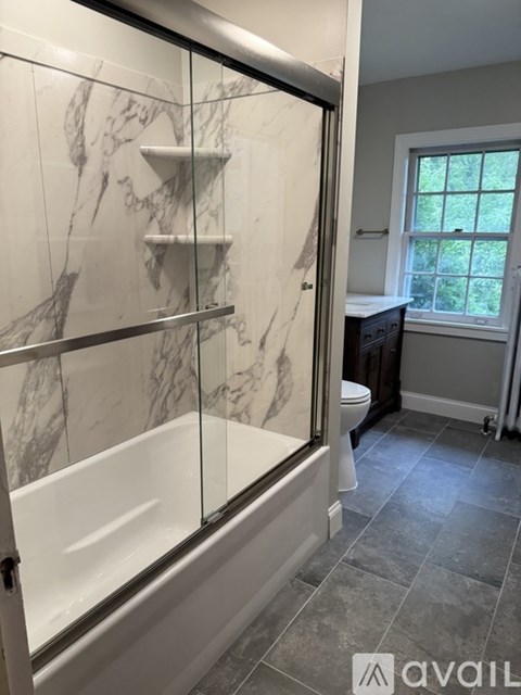 A bathroom with a marble tiled shower and a window.