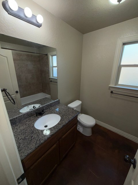 A bathroom with a toilet, sink, mirror, and lights.