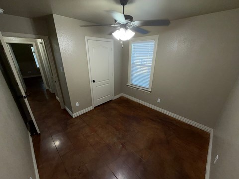 A room with a ceiling fan and brown flooring.