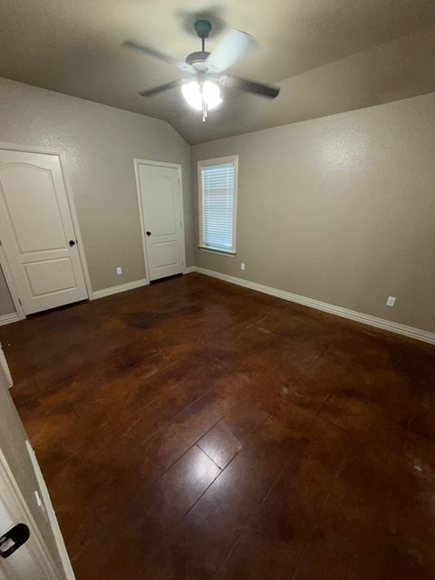 A room with brown flooring and a ceiling fan.