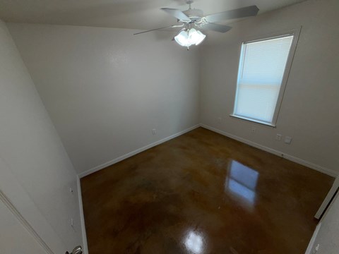 A room with a brown floor and a ceiling fan.