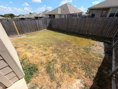 A backyard with a wooden fence and a grassy area.