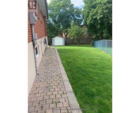 A backyard with a brick walkway leading to a white shed.
