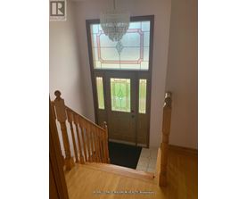 A stained glass window in a home with a wooden staircase.
