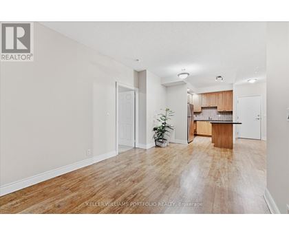 A room with a wooden floor and a kitchen area in the background.