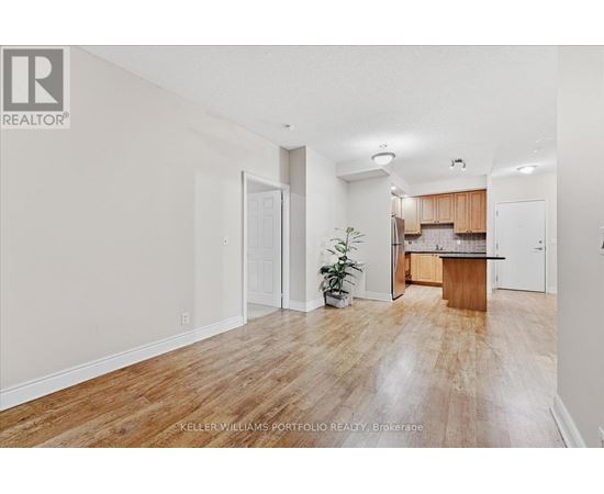 A room with a wooden floor and a kitchen area in the background.