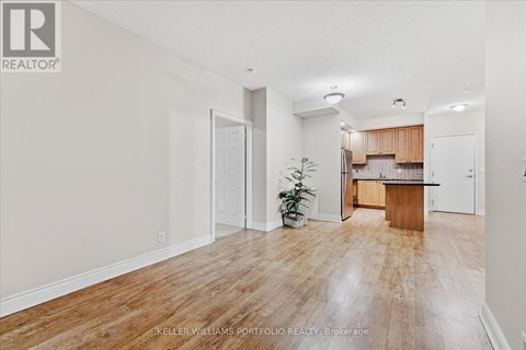 A room with a wooden floor and a kitchen area in the background.