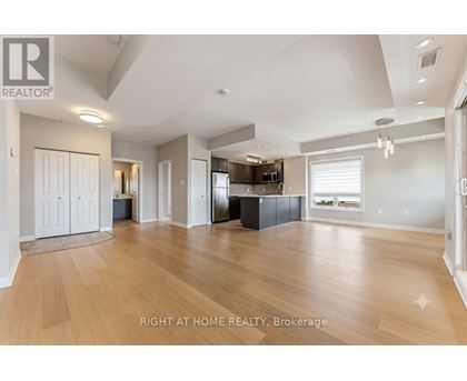 A spacious living room with wooden flooring and a kitchen area in the background.