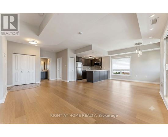 A spacious living room with wooden flooring and a kitchen area in the background.