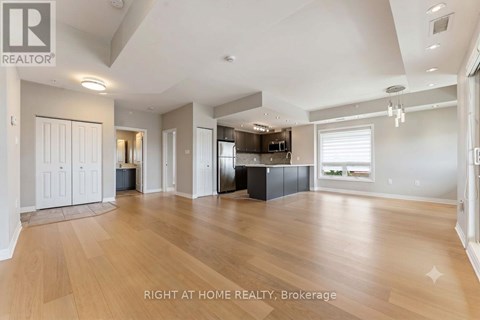 A spacious living room with wooden flooring and a kitchen area in the background.