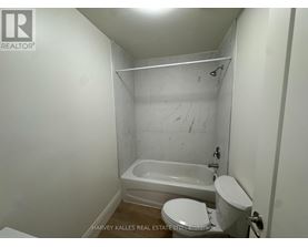 A white toilet sits next to a bathtub in a small bathroom.