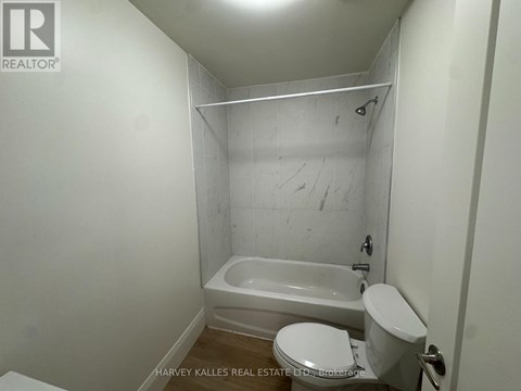 A white toilet sits next to a bathtub in a small bathroom.