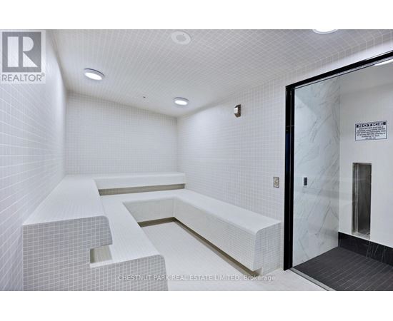 A white tiled bathroom with a glass door leading to a shower.
