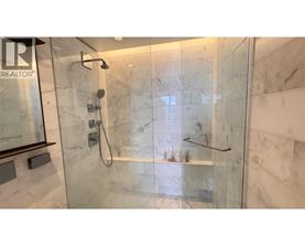 A shower area with a glass door and a marble wall.