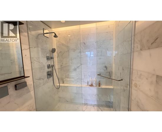 A shower area with a glass door and a marble wall.