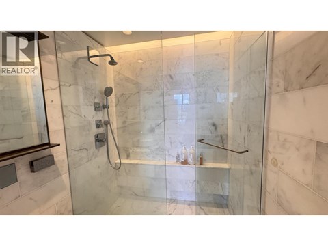 A shower area with a glass door and a marble wall.