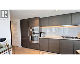 A modern kitchen with a glass table and a stainless steel refrigerator.