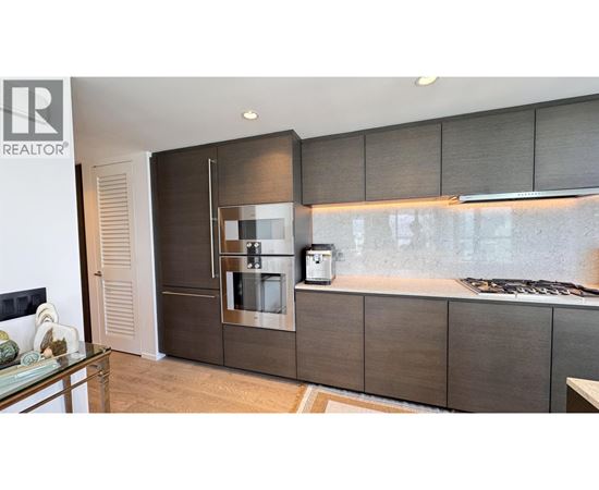 A modern kitchen with a glass table and a stainless steel refrigerator.