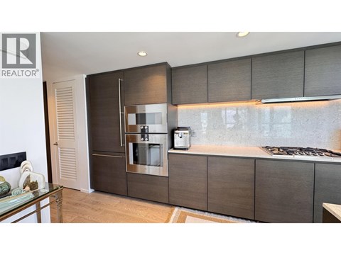A modern kitchen with a glass table and a stainless steel refrigerator.
