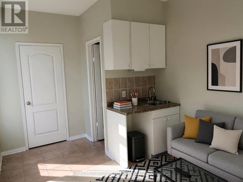 A living room with a grey couch and a kitchenette.