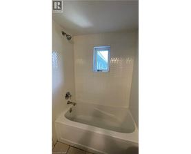 A white bathtub in a bathroom with a window above it.