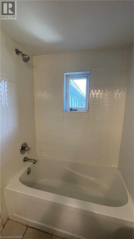 A white bathtub in a bathroom with a window above it.