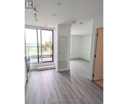 A spacious room with wooden flooring and a large window overlooking a balcony.