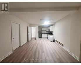 A long, empty hallway with a white door on the left and a kitchen area visible in the distance.