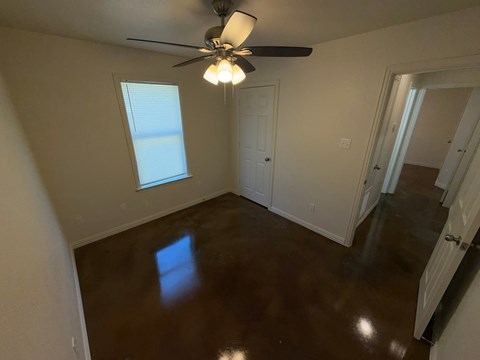 A room with a ceiling fan and brown flooring.