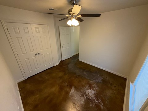 A room with a brown floor and a ceiling fan.