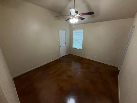 A room with a ceiling fan and brown flooring.