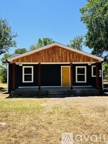 A small black and brown house with a yellow door stands alone in a grassy field.