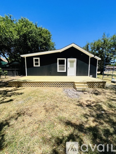 A small black house with a white door and windows is surrounded by a grassy area.