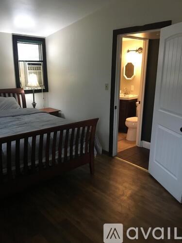 A bedroom with a bed, a nightstand with a lamp, and a doorway leading to a bathroom.
