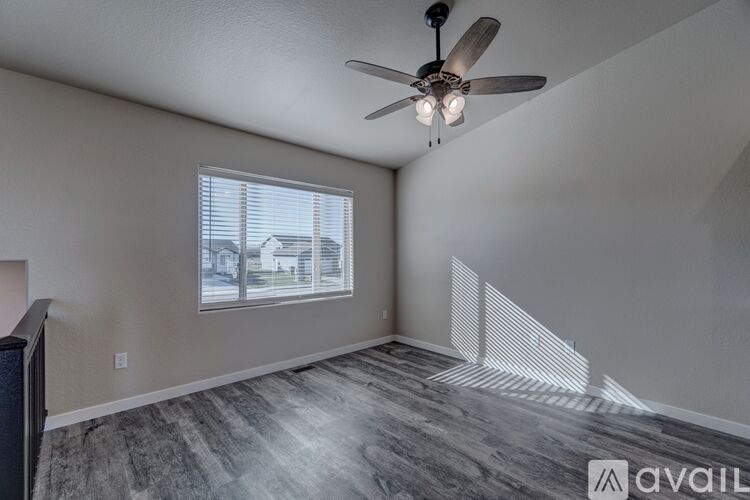 A room with a ceiling fan and a window overlooking a house.