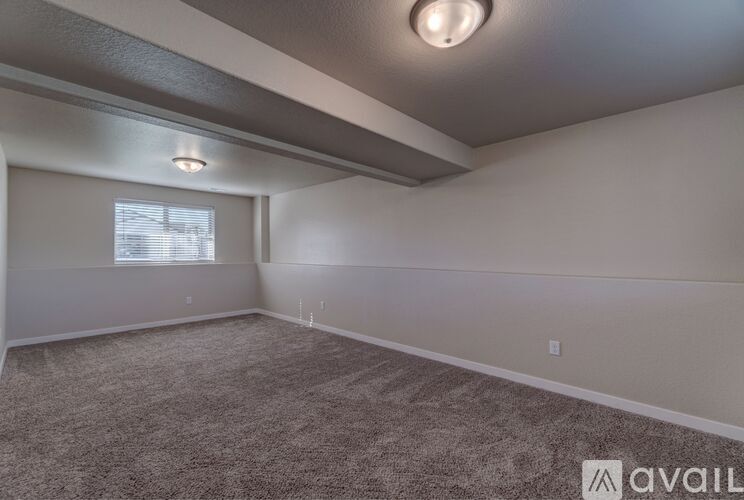 A spacious room with a carpeted floor and a window with blinds.