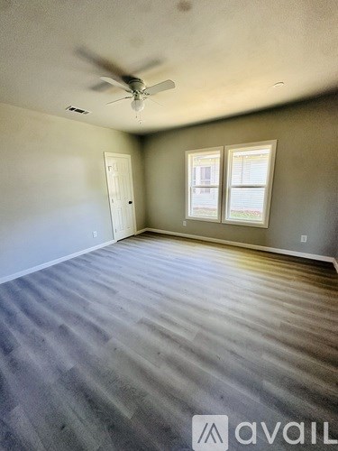 A room with a ceiling fan and two windows.