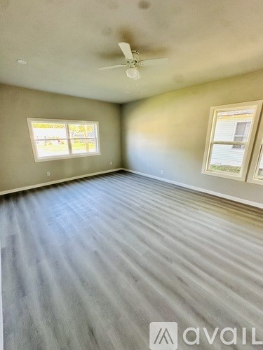 A room with a ceiling fan and two windows.