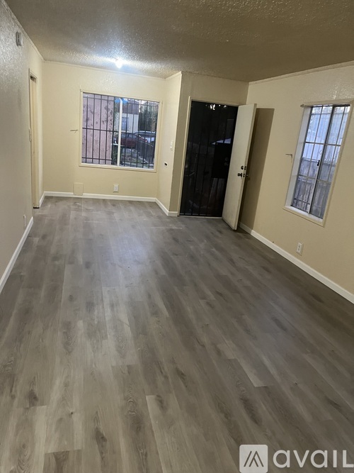 A spacious room with wooden flooring and a black door.
