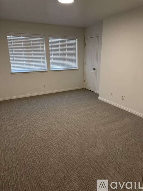 A room with carpeted floor, two windows with blinds, and a door.
