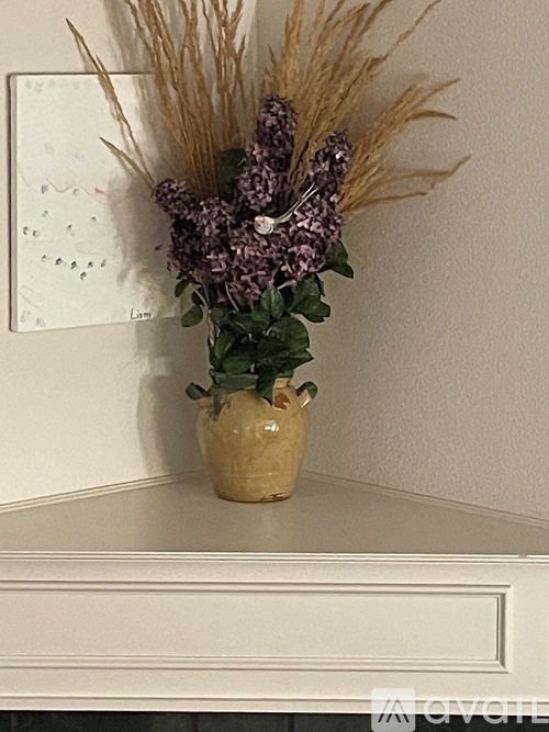 A vase with purple flowers and dried grasses sits on a white shelf.