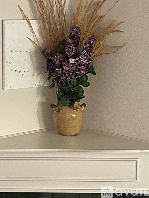 A vase with purple flowers and dried grasses sits on a white shelf.