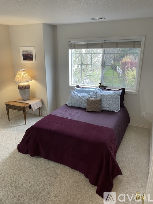 A bedroom with a purple bedspread and a lamp on a side table.